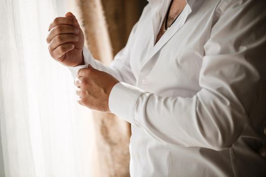 Man businessman buttoning a button on the sleeve of a white dress shirt