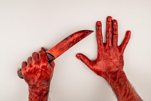 A man with bloody hands holds a knife on a white background