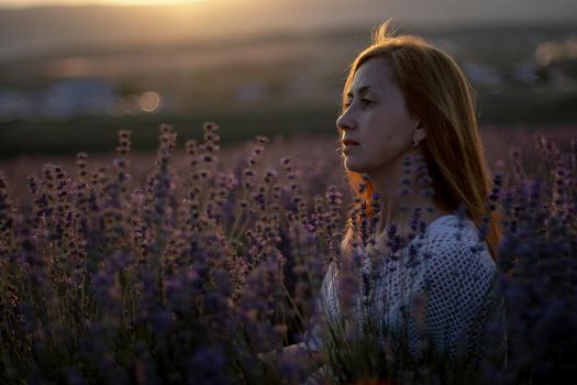 A middle-aged woman sits in a lavender field and enjoys aromatherapy. Aromatherapy concept, lavender oil, photo session in lavender.