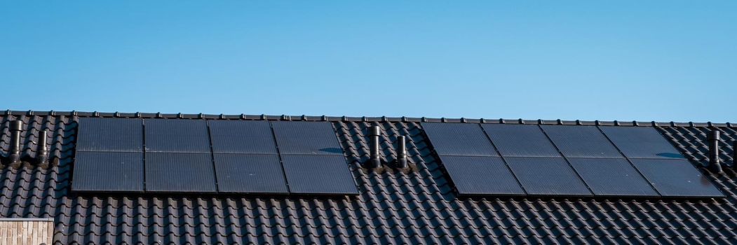 Newly build houses with solar panels attached on the roof against a sunny sky Close up of a new building with black solar panels. Zonnepanelen, Zonne energie, Translation: Solar panel, , Sun Energy.