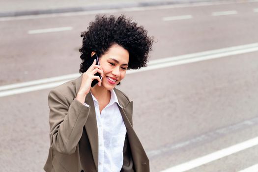 portrait of a smiling latin business woman walking by the street talking by phone, concept of urban lifestyle and success, copy space for text