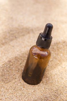 Cosmetic serum for the skin in a glass bottle. A bottle with a pipette on a sandy beach by the sea. Essences for skin care on a sandy background. The concept of natural cosmetics and SPA products.