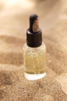 Cosmetic serum for the skin in a glass bottle. A bottle with a pipette on a sandy beach by the sea. Essences for skin care on a sandy background. The concept of natural cosmetics and SPA products.
