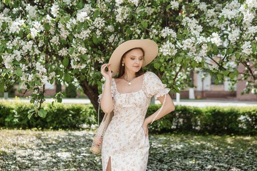 An attractive long-haired woman walks in the spring in the park of blooming apple trees. Spring portrait of a woman