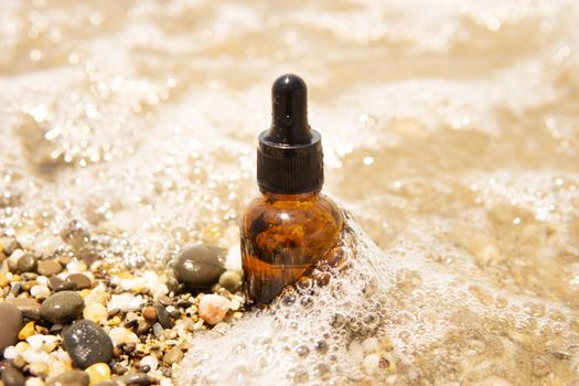 Cosmetic serum for the skin in a glass bottle. A bottle with an eyedropper on a pebble beach by the sea. Essences for skin care on the background of stones. The concept of natural cosmetics and SPA products.