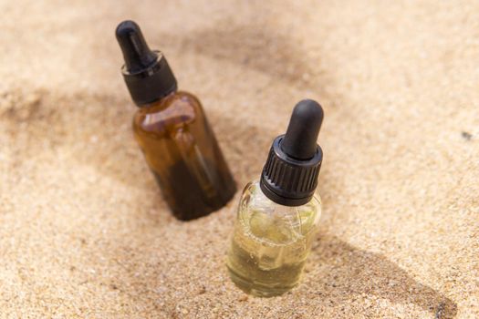 Cosmetic serum for the skin in a glass bottle. A bottle with a pipette on a sandy beach by the sea. Essences for skin care on a sandy background. The concept of natural cosmetics and SPA products.