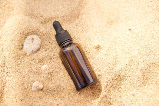 Cosmetic serum for the skin in a glass bottle. A bottle with a pipette on a sandy beach by the sea. Essences for skin care on a sandy background. The concept of natural cosmetics and SPA products.