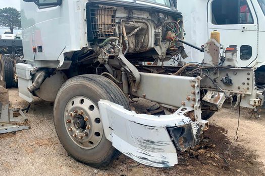 An abandoned truck in a junkyard, a white lorry with a destroyed engine and bumper after a head-on collision on the road, big broken automobile on a car dump