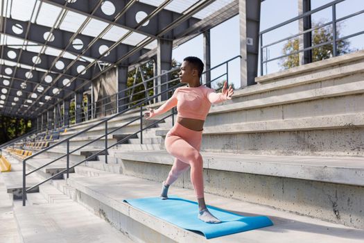 African American woman doing yoga near the stadium in the morning, active lifestyle performs fitness exercises