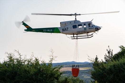 firefighting helicopter in mid-flight dropping water bag on flames