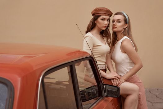 Young beautiful girls dressed in retro vintage style enjoying the old european city summertime lifestyle. Women posing by an old car.