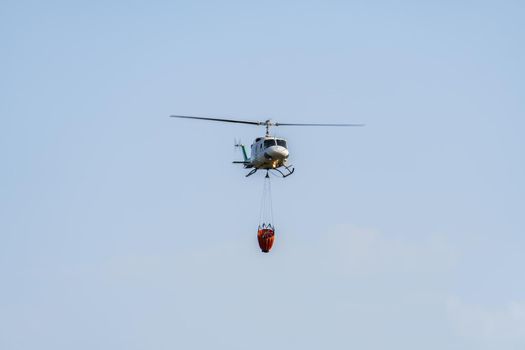 firefighting helicopter in mid-flight dropping water bag on flames