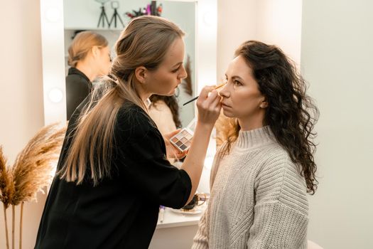 Make-up artist makes a professional make-up of a young woman in the studio