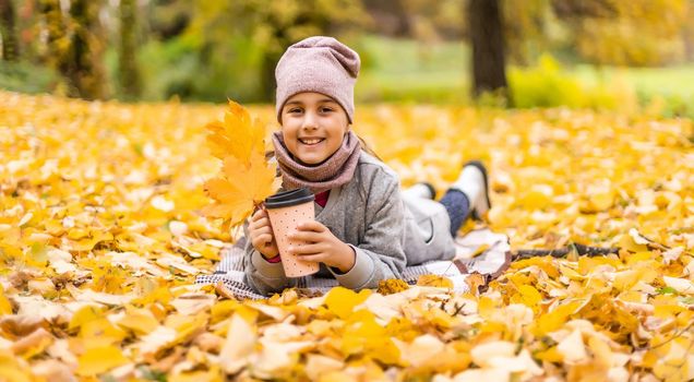 Little funny girl lies on yellow leaves in the forest. Child on a walk in the autumn park.