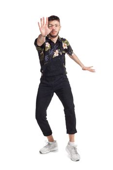 Full-length photo of a good-looking dancer in glasses, black jumpsuit, funny dark t-shirt and sneakers fooling around in studio. Indoor photo of a male dancing isolated on white background. Music and imagination.