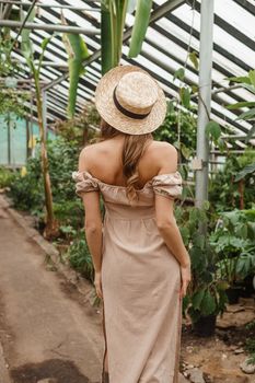 A beautiful young woman takes care of plants in a greenhouse. The concept of gardening and an eco-friendly lifestyle.