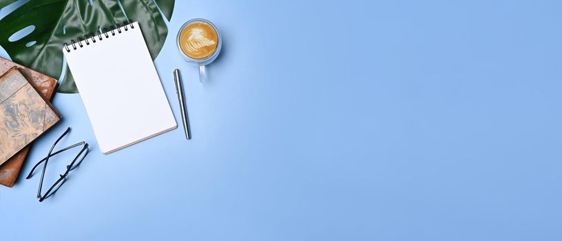 Top view empty notebook, coffee cup and glasses on blue background.