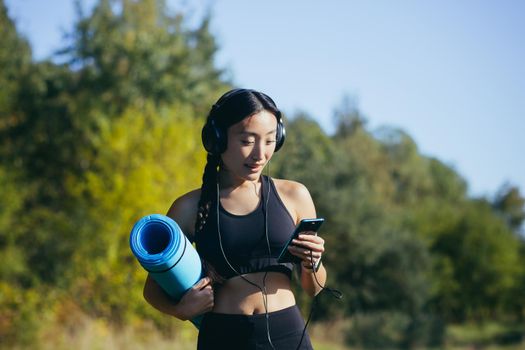 Beautiful asian woman athlete goes to fitness class, listens to music on headphones and uses the phone