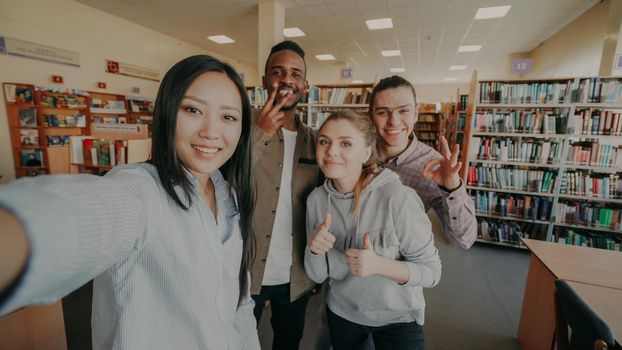 Point of view of international student group have fun smiling and taking selfie photos on smartphone camera at university library indoors