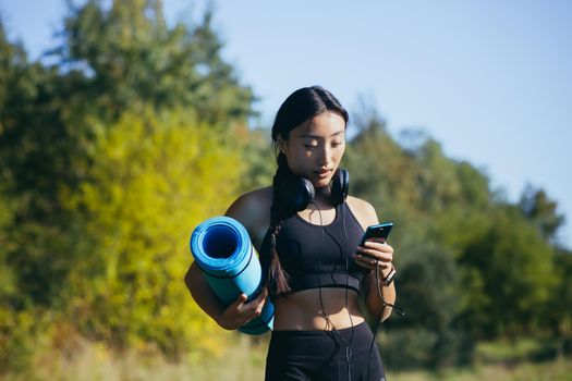 Beautiful asian woman athlete goes to fitness class, listens to music on headphones and uses the phone