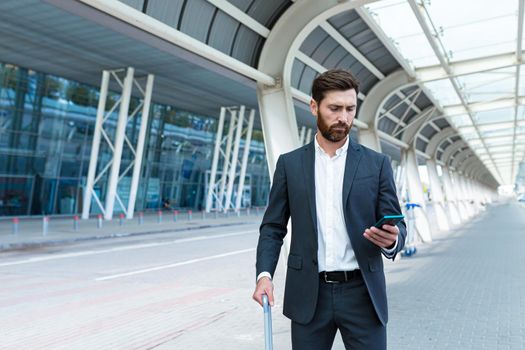 business man standing background a modern train station airport or bus stop in formal suit with a suitcase using app mobile phone Traveling businessman tourist with a smartphone in hands order a taxi