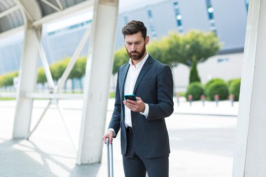 business man standing background a modern train station airport or bus stop in formal suit with a suitcase using app mobile phone Traveling businessman tourist with a smartphone in hands order a taxi