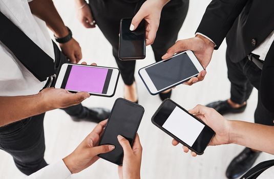 Get connected and stay updated. Closeup shot of a group of unrecognisable businesspeople using cellphones together in an office