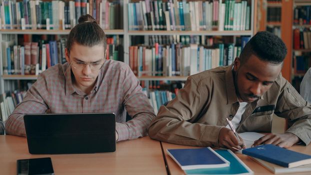 Two concentrated students preparing for examination while sitting at table in university library indoors