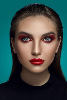 Close-up glamour portrait of a beautiful woman with bright smoky eyes make-up and long blond hair, dressed in a black turtleneck, looking at the camera while posing over a gray background. Fashion shiny highlighter on her skin, sexy red lips and dark eyebrows.