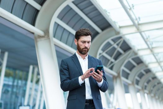 business man standing background a modern train station airport or bus stop in formal suit with a suitcase using app mobile phone Traveling businessman tourist with a smartphone in hands order a taxi