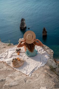 Street photo of a beautiful woman with dark hair in a mint dress and hat having a picnic on a hill overlooking the sea