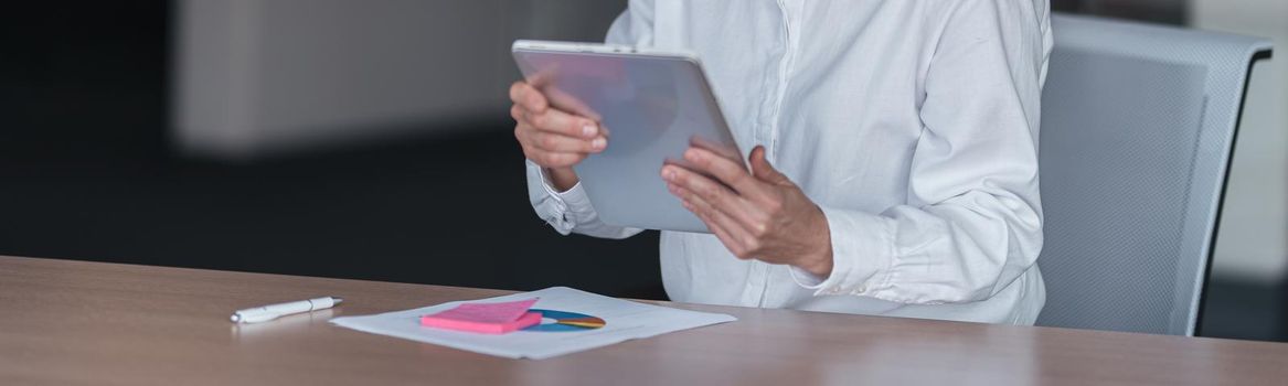 Smiling businesswoman with glasses working on digital tablet at her workplace in modern office.