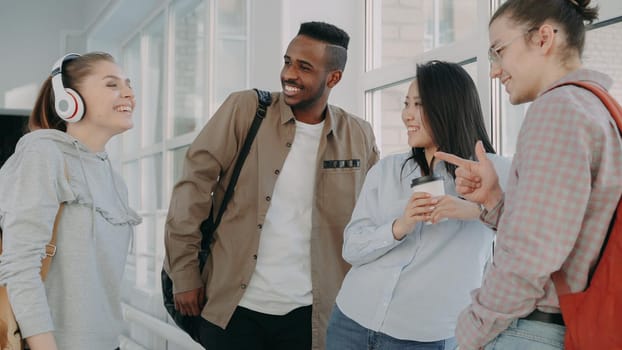 view of multi-ethnic group of students standing together in corridor of college. Beautiful caucasian girl is standing on front of them explaining and gesturing.