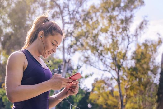 attractive blonde sports woman smile while listening music before workout outdoors at park, fitness accessories