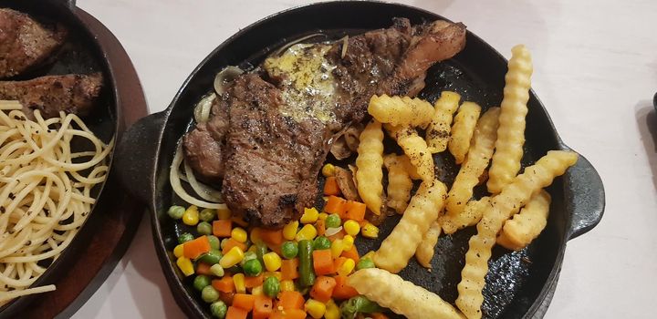 The best food in the world beef steak along with fried potatoes with delicious mushroom sauce and salad and spaghetti plated in beautiful black plate