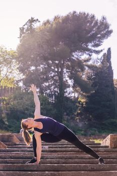 beautiful young woman doing yoga exercise on the stairs of the park, morning workout outdoors, sports and healthy lifestyle