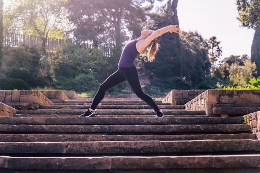 beautiful young woman doing yoga exercises on the stairs of the park, morning workout outdoors, sports and healthy lifestyle