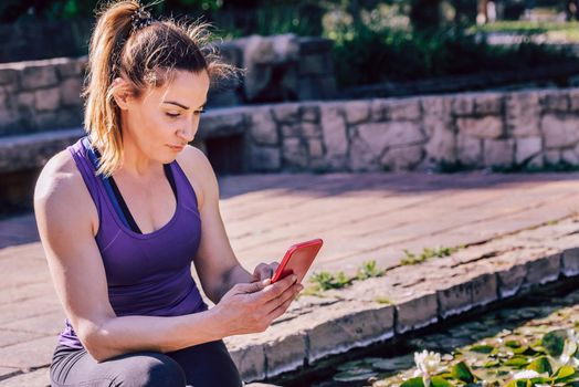 young sporty woman sitting writing at the phone at park, technology at sports and healthy lifestyle