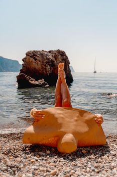 A young woman lies on the beach with her legs pointing to the sky, covering her body with a wide-brimmed straw hat. She is sunbathing on the ocean. The concept of vacation, travel, vacation