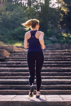 young sporty woman running upstairs in the morning on the stairs of the park, morning workout outdoors, sports and healthy lifestyle