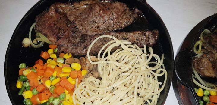 The best food in the world beef steak along with fried potatoes with delicious mushroom sauce and salad and spaghetti plated in beautiful black plate