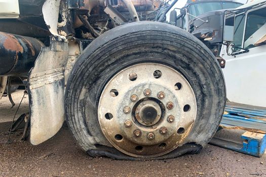 Closeup of wrecked truck wheel with a punctured or flat tire at a car junkyard after a traffic accident