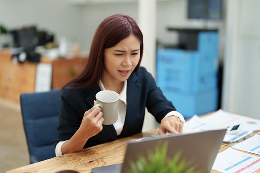 Asian businesswoman taking a coffee break while using a computer.