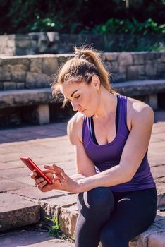 young sporty woman sitting looking at the phone at park, technology at sports and healthy lifestyle