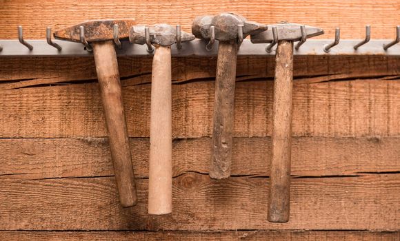 Four old hammers hang on a wooden wall in a garage. Garage wall-mounted storage system
