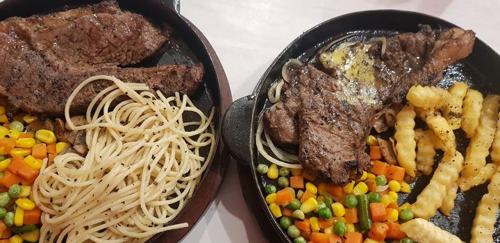 The best food in the world beef steak along with fried potatoes with delicious mushroom sauce and salad and spaghetti plated in beautiful black plate