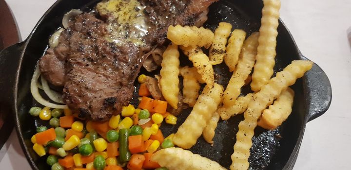 The best food in the world beef steak along with fried potatoes with delicious mushroom sauce and salad and spaghetti plated in beautiful black plate