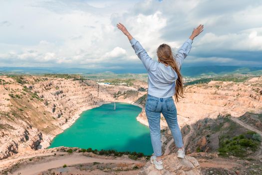 Girl on top of a mountain with raised hands, view of the azure lake in the form of a heart behind.