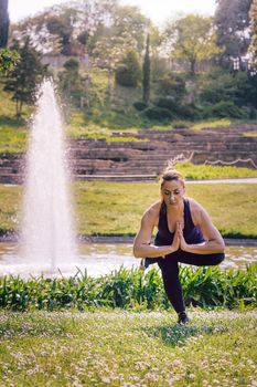 vertical photo of a young sports woman doing meditation yoga balancing exercises and relaxing outdoors in the park, modern healthy lifestyle and sport concept