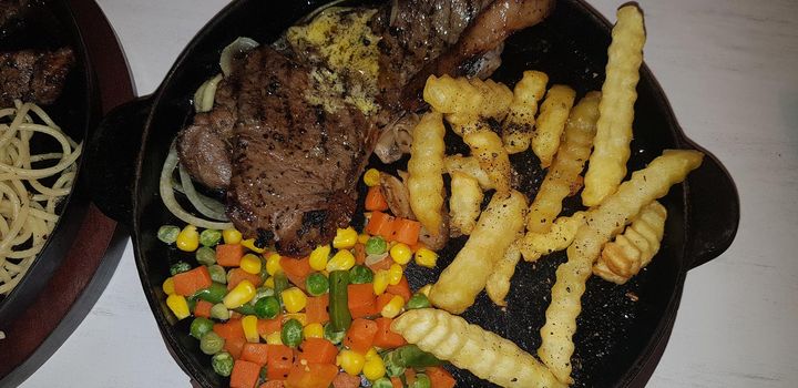 The best food in the world beef steak along with fried potatoes with delicious mushroom sauce and salad and spaghetti plated in beautiful black plate